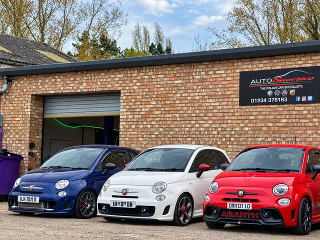 Three Abarth-badged Fiat 500s in blue, white and red outside the workshop