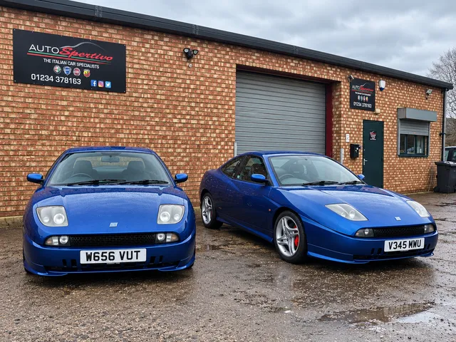 A pair of blue Fiat Coupes outside the workshop